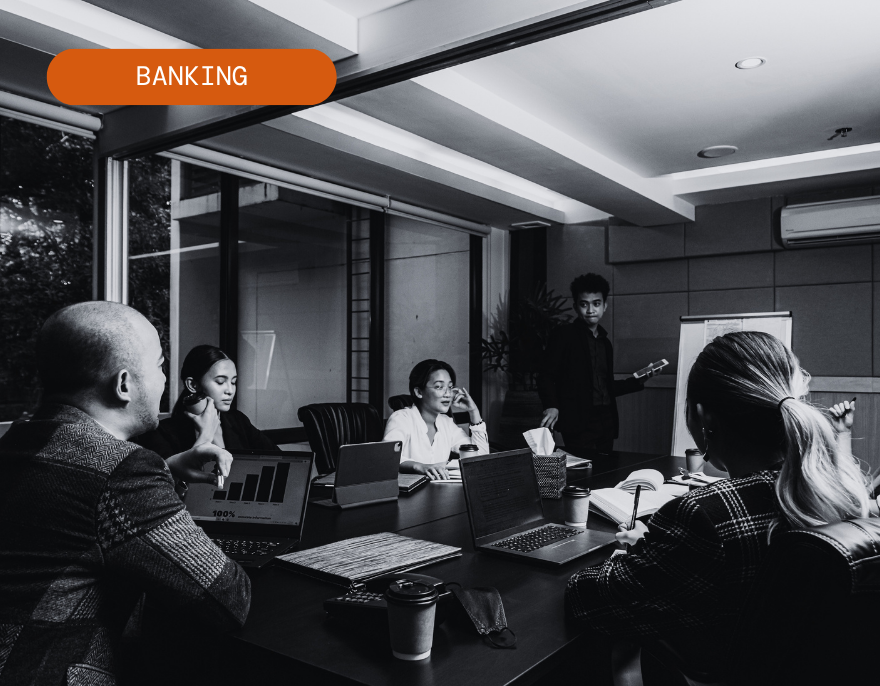 Banking team meeting in a conference room, with laptops and documents around a table.