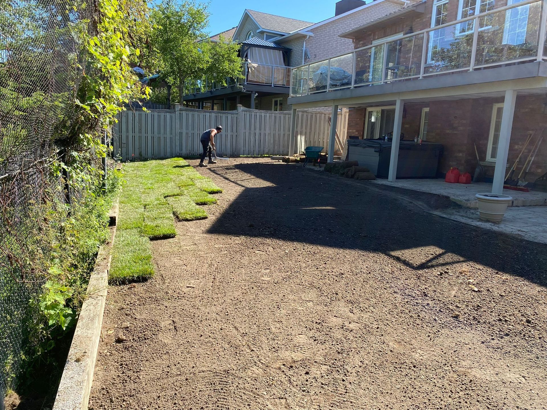 A man is standing in a backyard installing sod