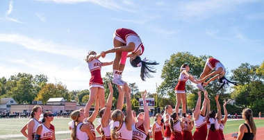 Cheerleader in red uniform performs a backbend on a green and red football field.