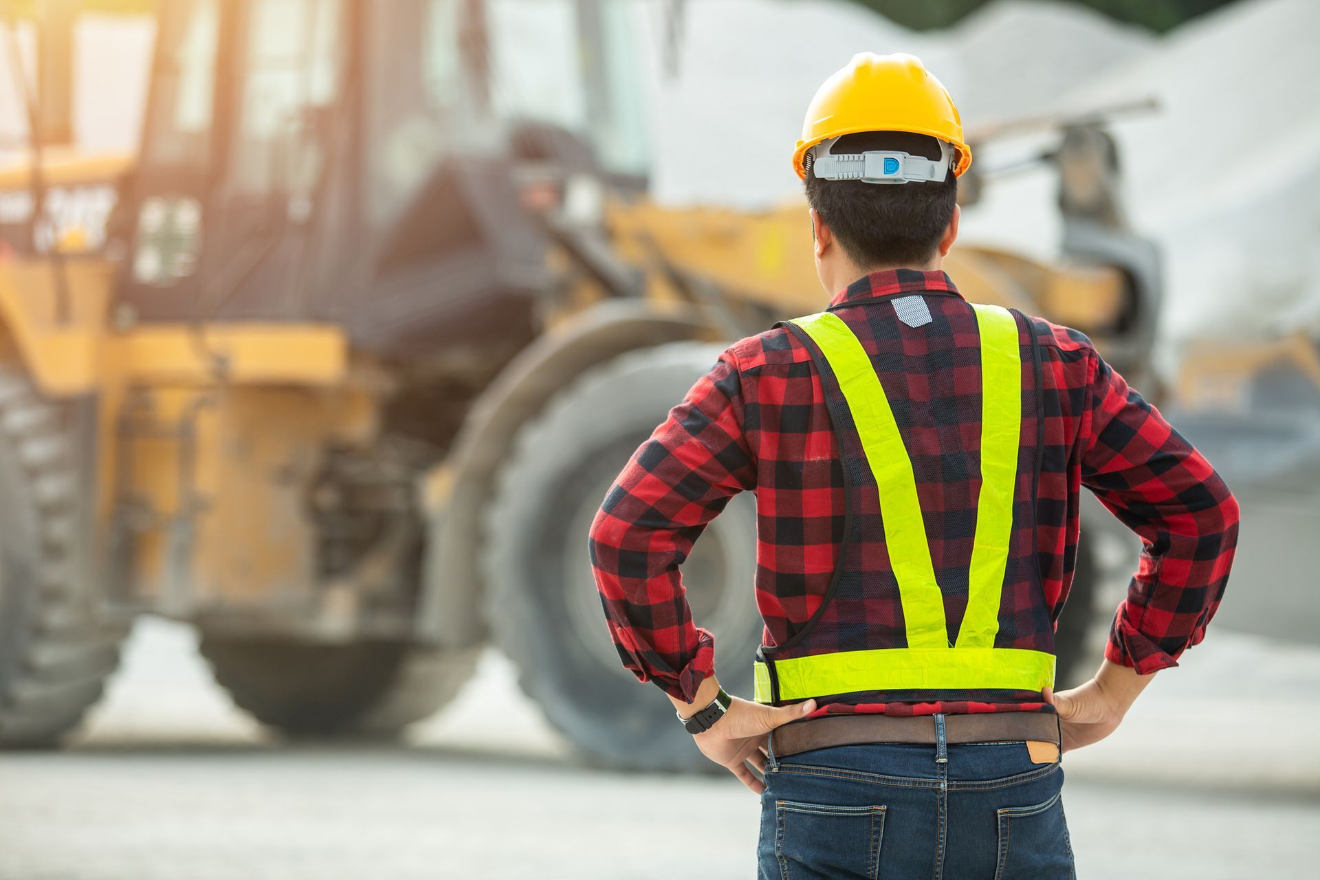 A construction worker wearing a hard hat and safety vest is standing in front of a bulldozer.