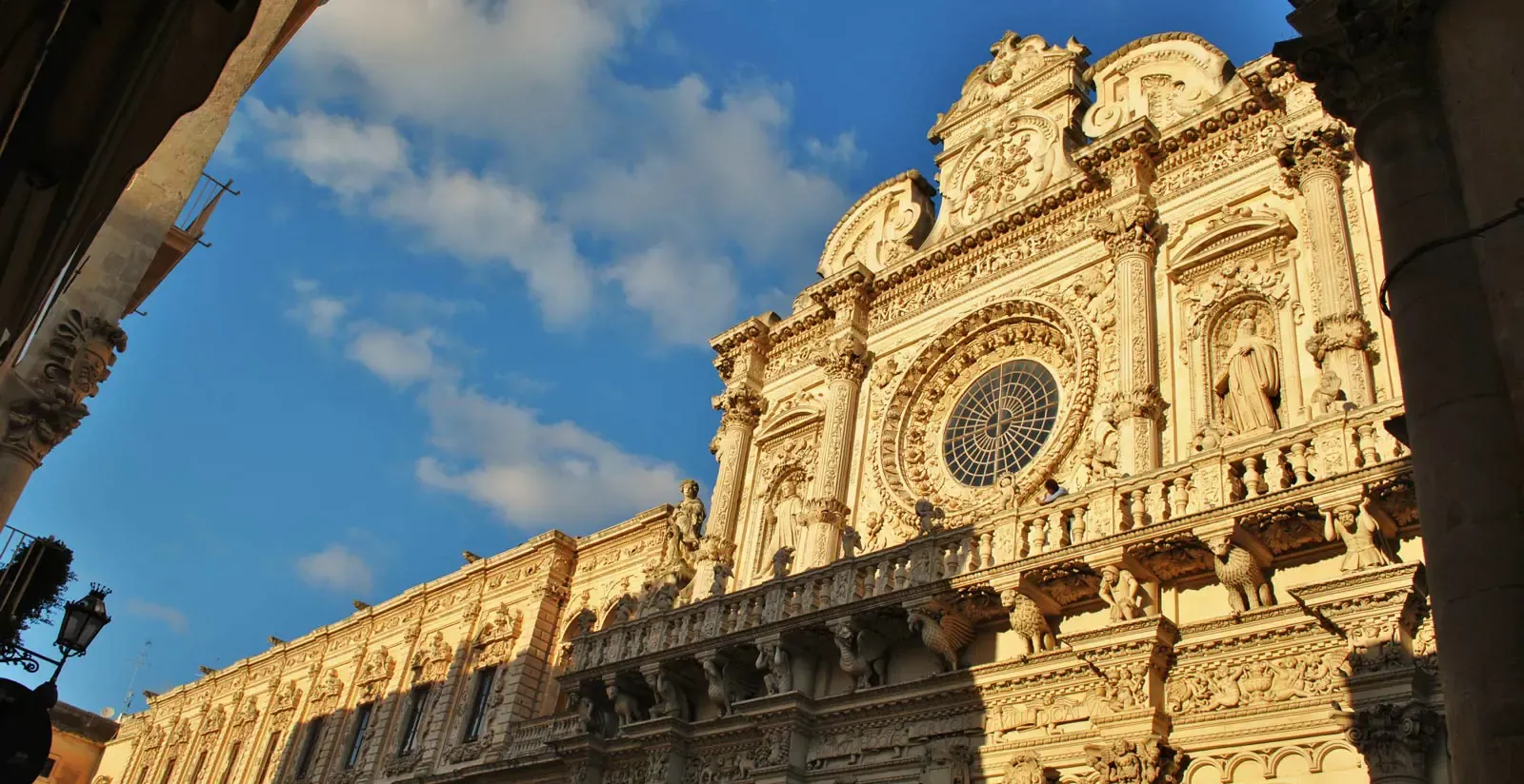 Ornate baroque facade of a church in Lecce, Italy, against a blue sky with clouds.