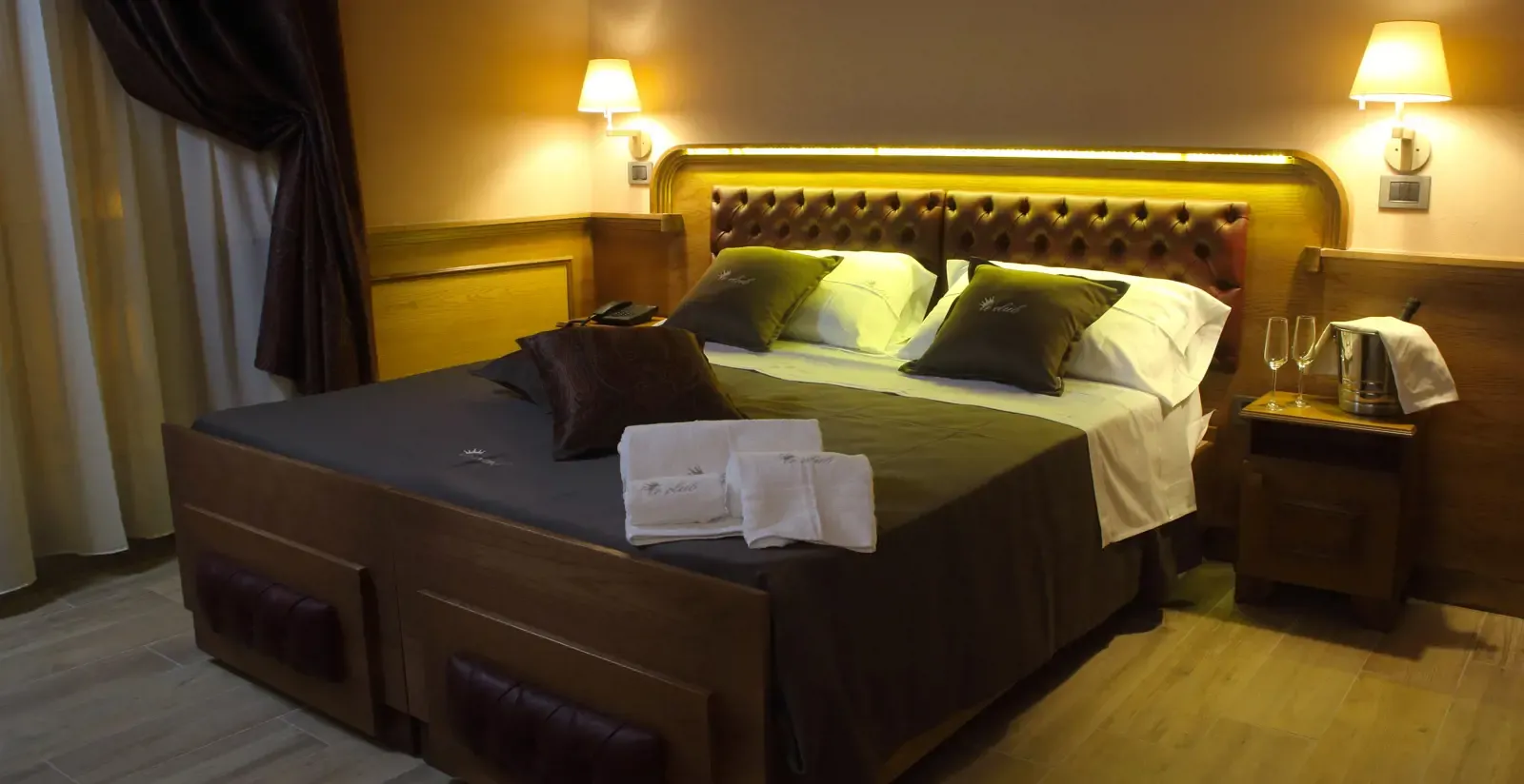 Bedroom with a large bed, brown headboard, nightstand with champagne, and warm lighting.