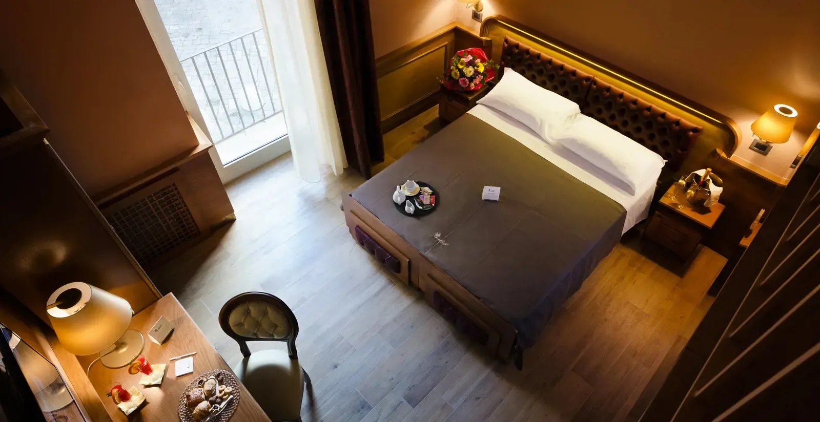 Camera da letto con letto, scrivania e sedia. Illuminazione calda, tonalità marroni, finestra con tende.