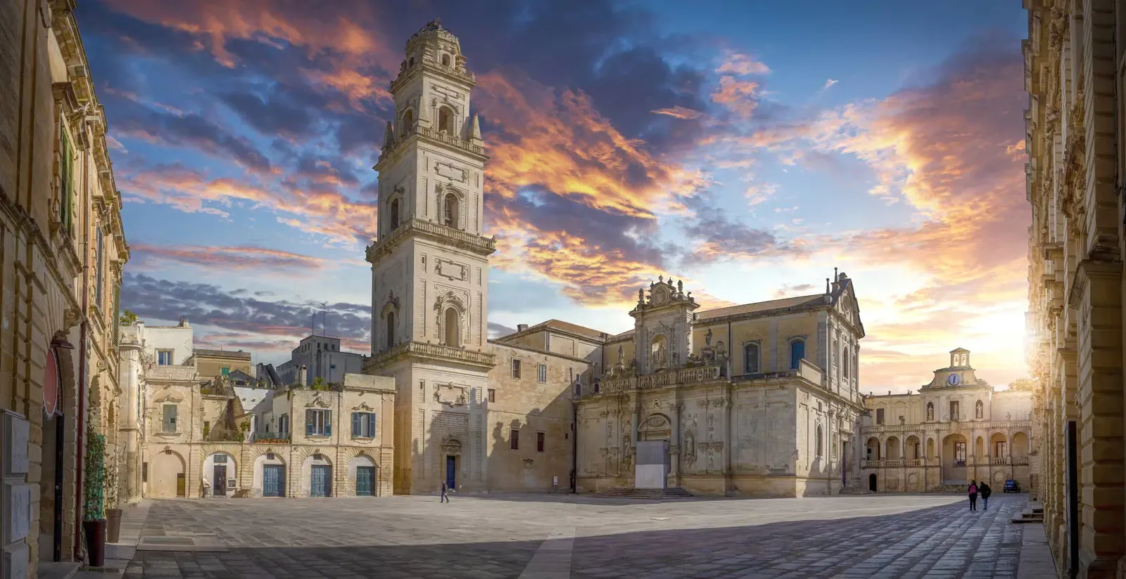 Una chiesa alta e decorata in una piazza cittadina italiana sullo sfondo di un tramonto vibrante.