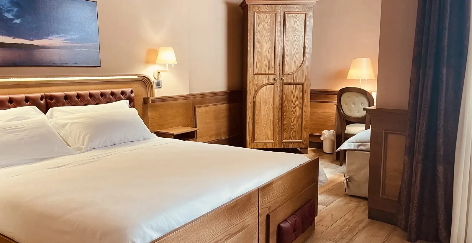 Bedroom with a large bed, wooden wardrobe, desk, and two lamps.