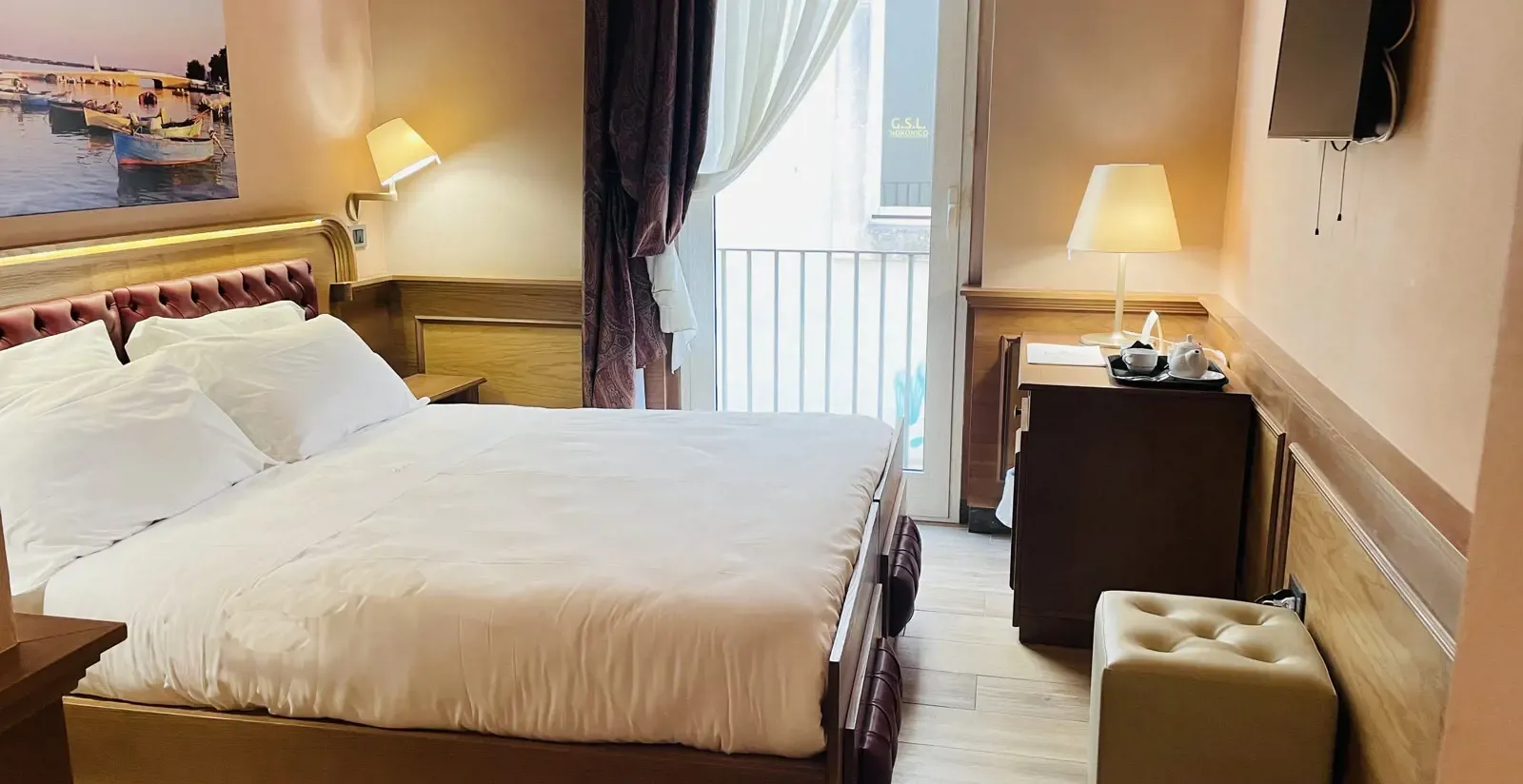 Hotel room with a bed, desk, lamps, and a balcony with curtains.