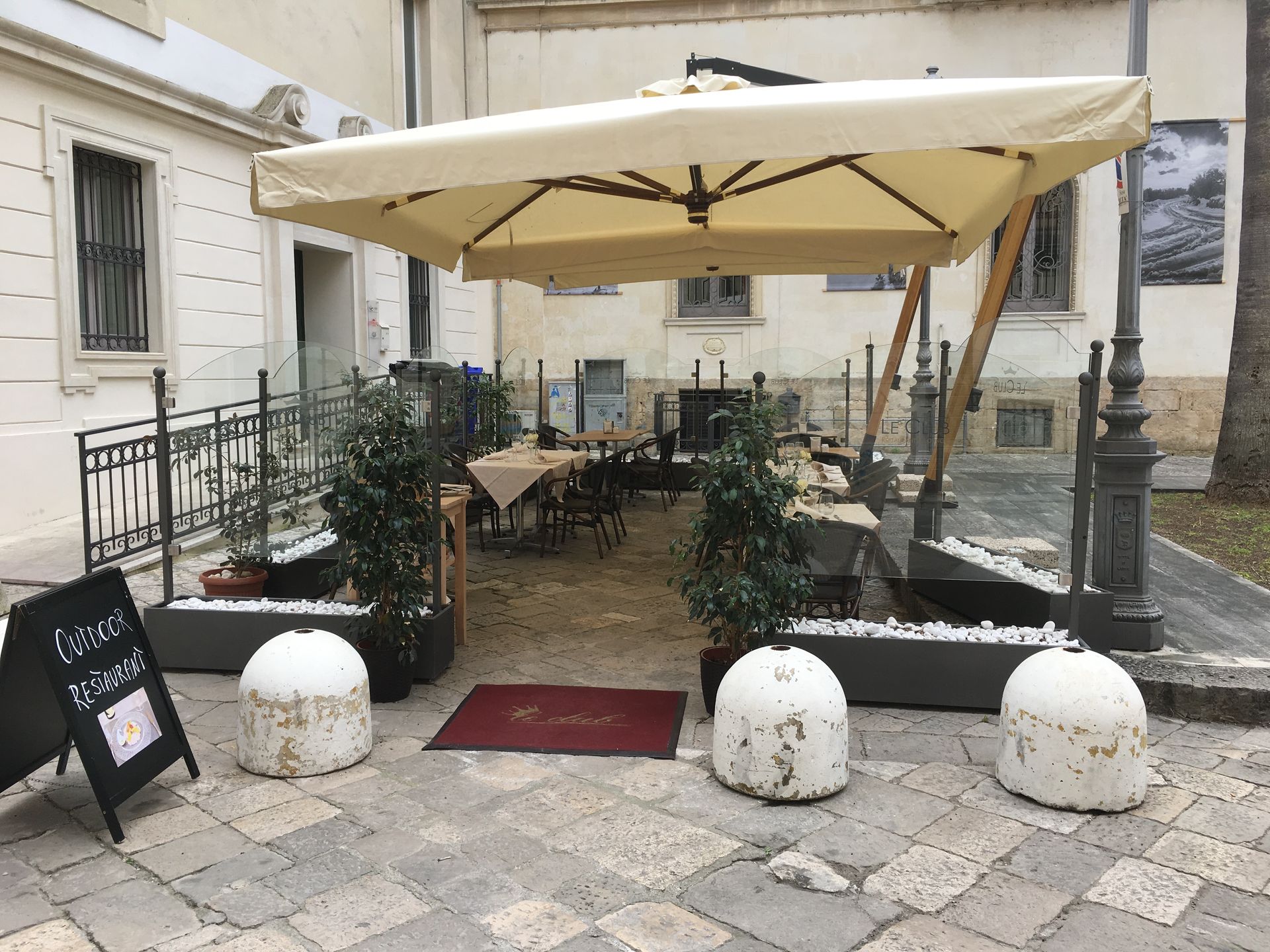 Outdoor restaurant seating area with tables under a beige umbrella.
