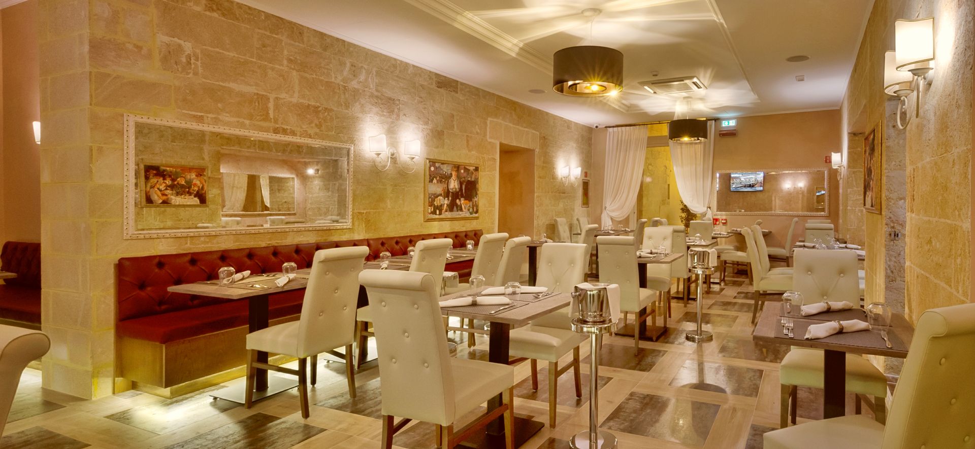 Restaurant interior with stone walls, red booth seating, and white chairs around tables.