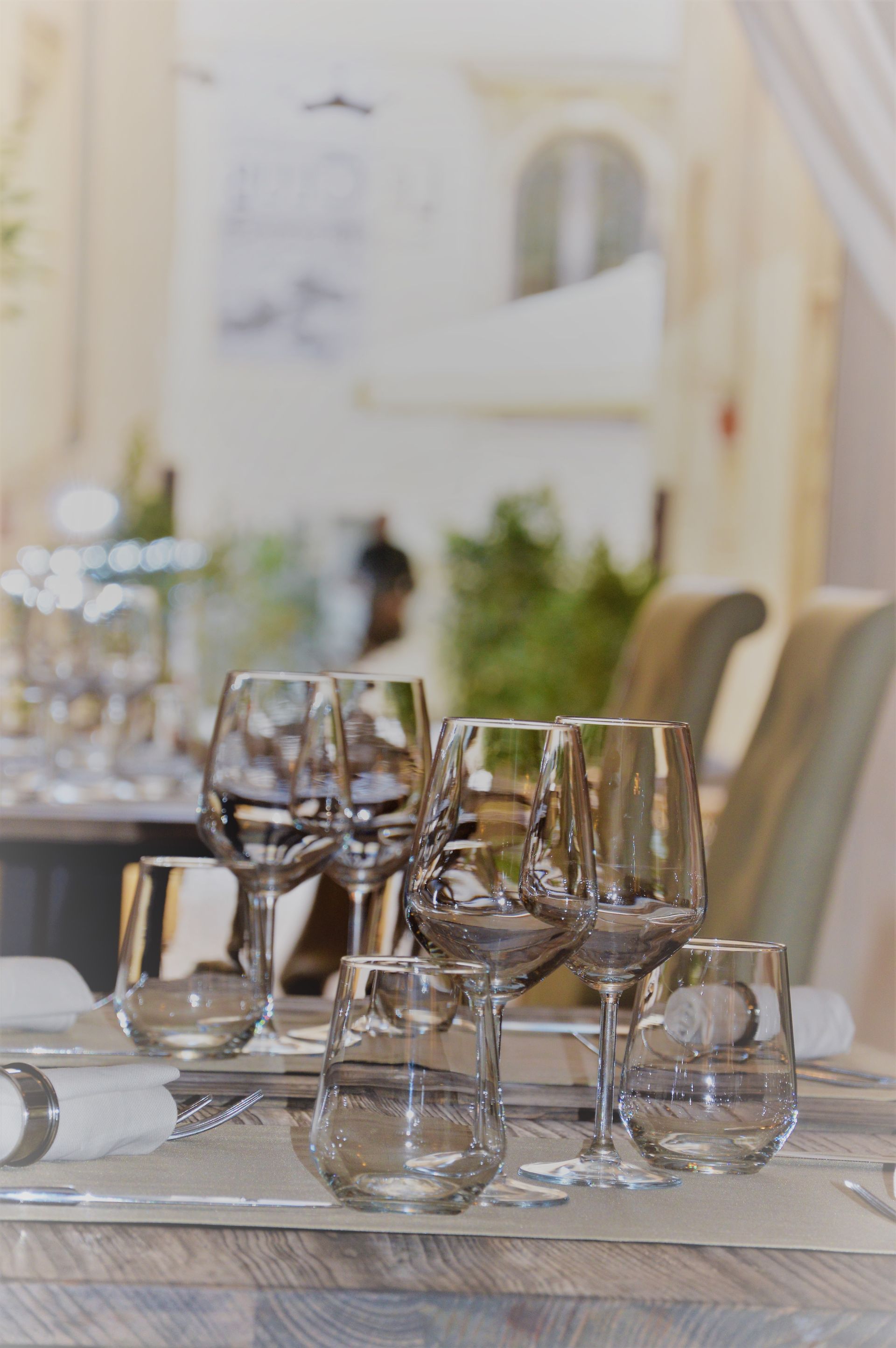 Table setting with wine glasses, water glasses, and place settings. Soft lighting, blurred background of a restaurant.