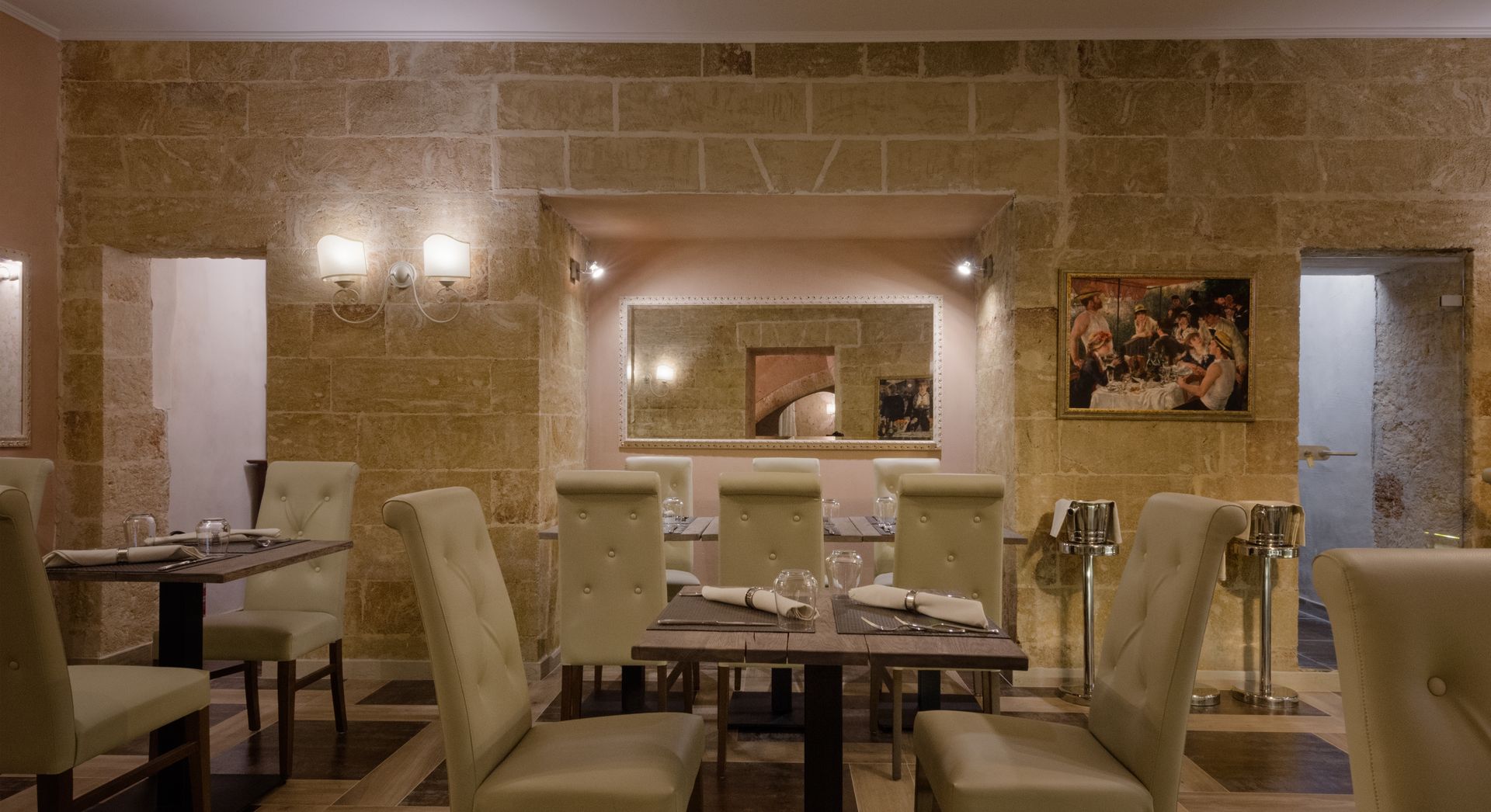 Restaurant interior with stone walls, tables, chairs, mirror, and artwork.