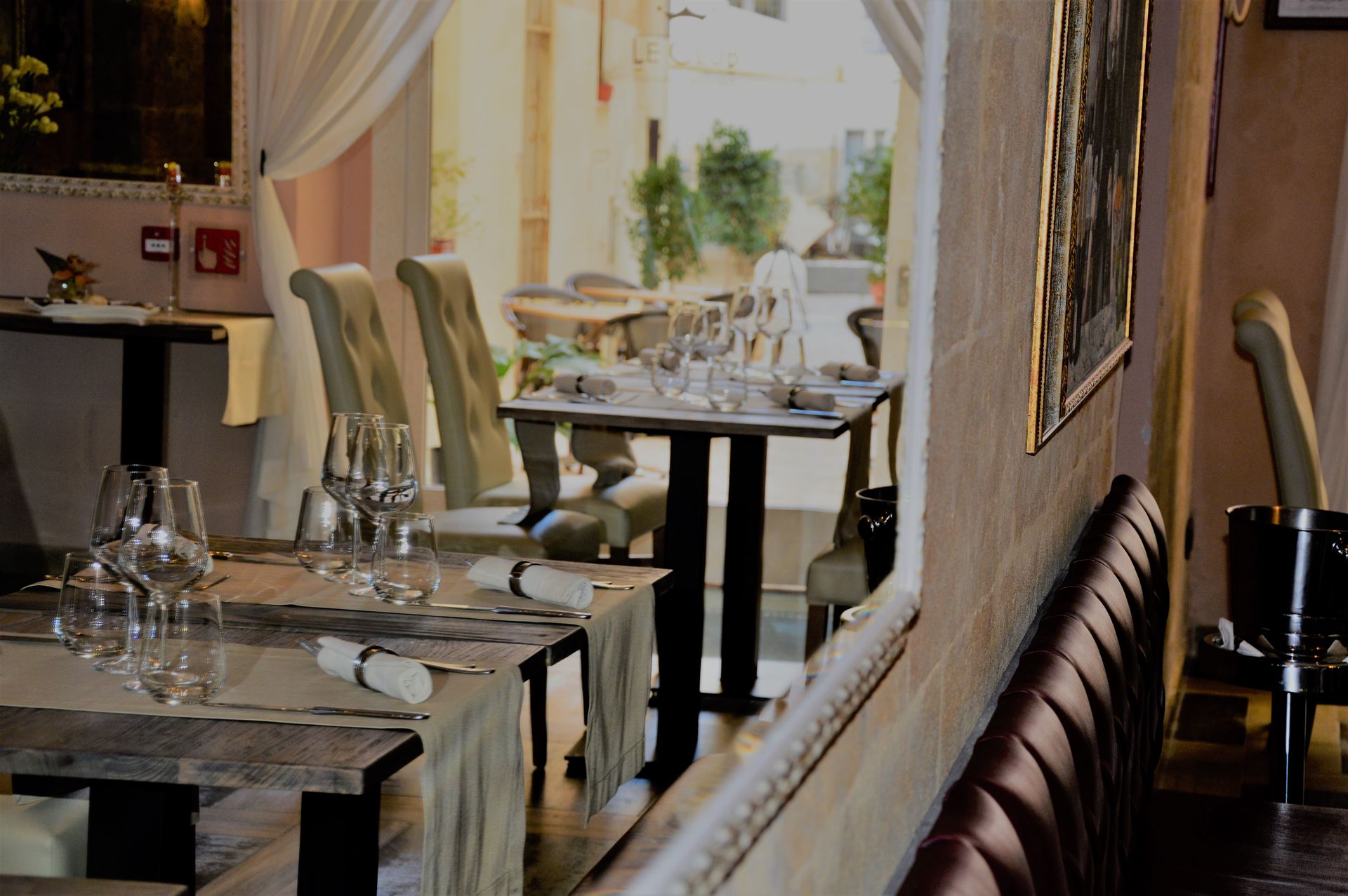 Restaurant interior with tables set for dining, view of a courtyard through an archway.