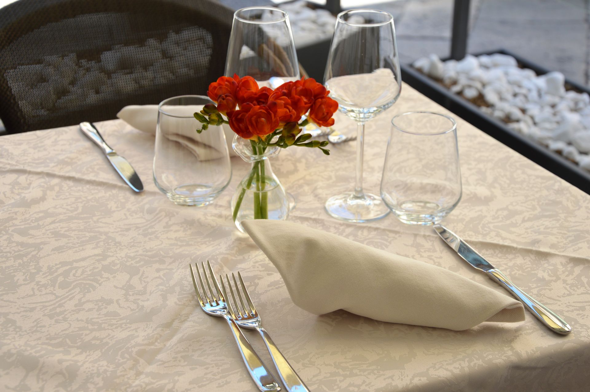 Table set for dining with flowers, glasses, and silverware on a cream-colored tablecloth.