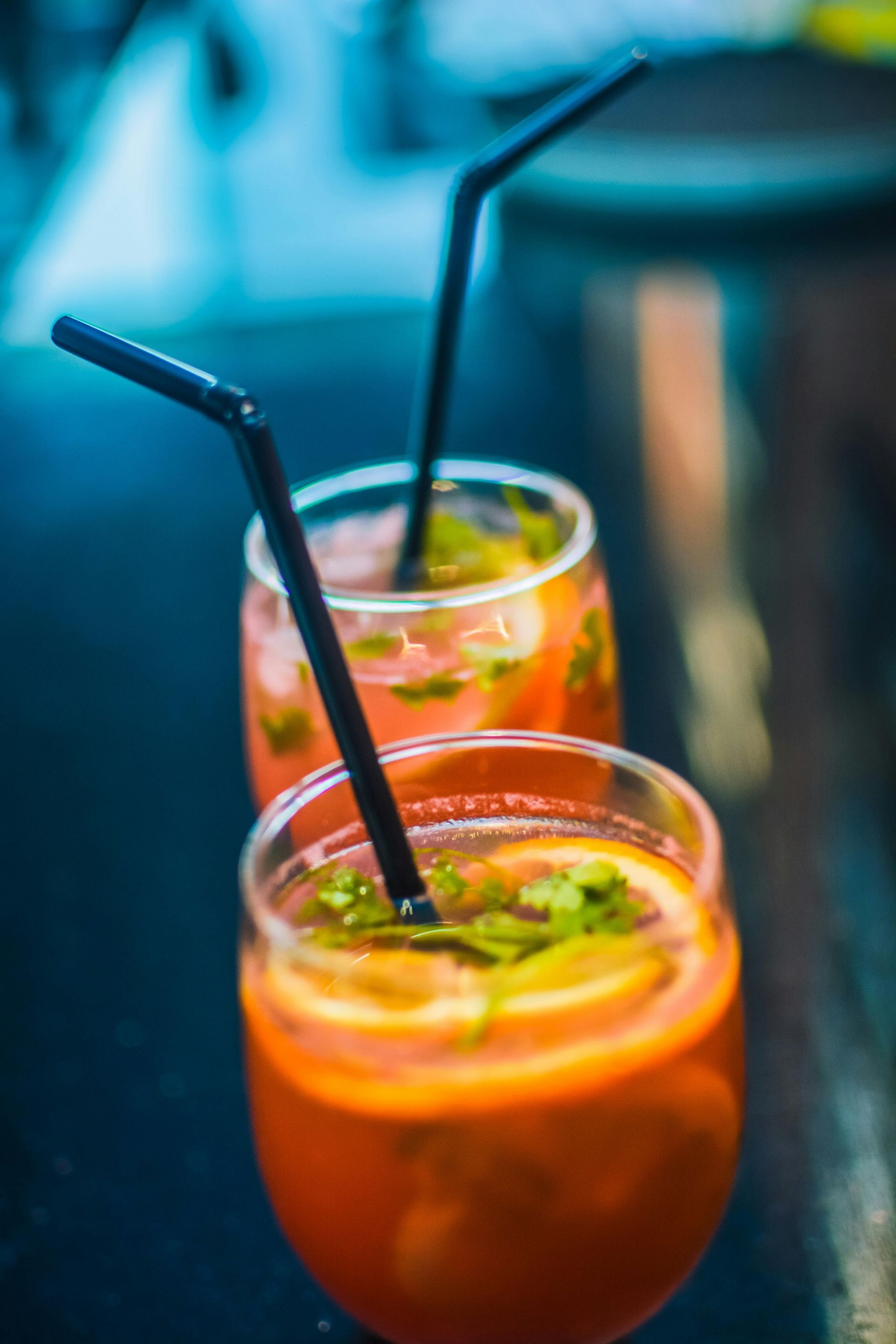 Due cocktail all'arancia con cannucce nere, guarniti con menta e fette d'arancia.