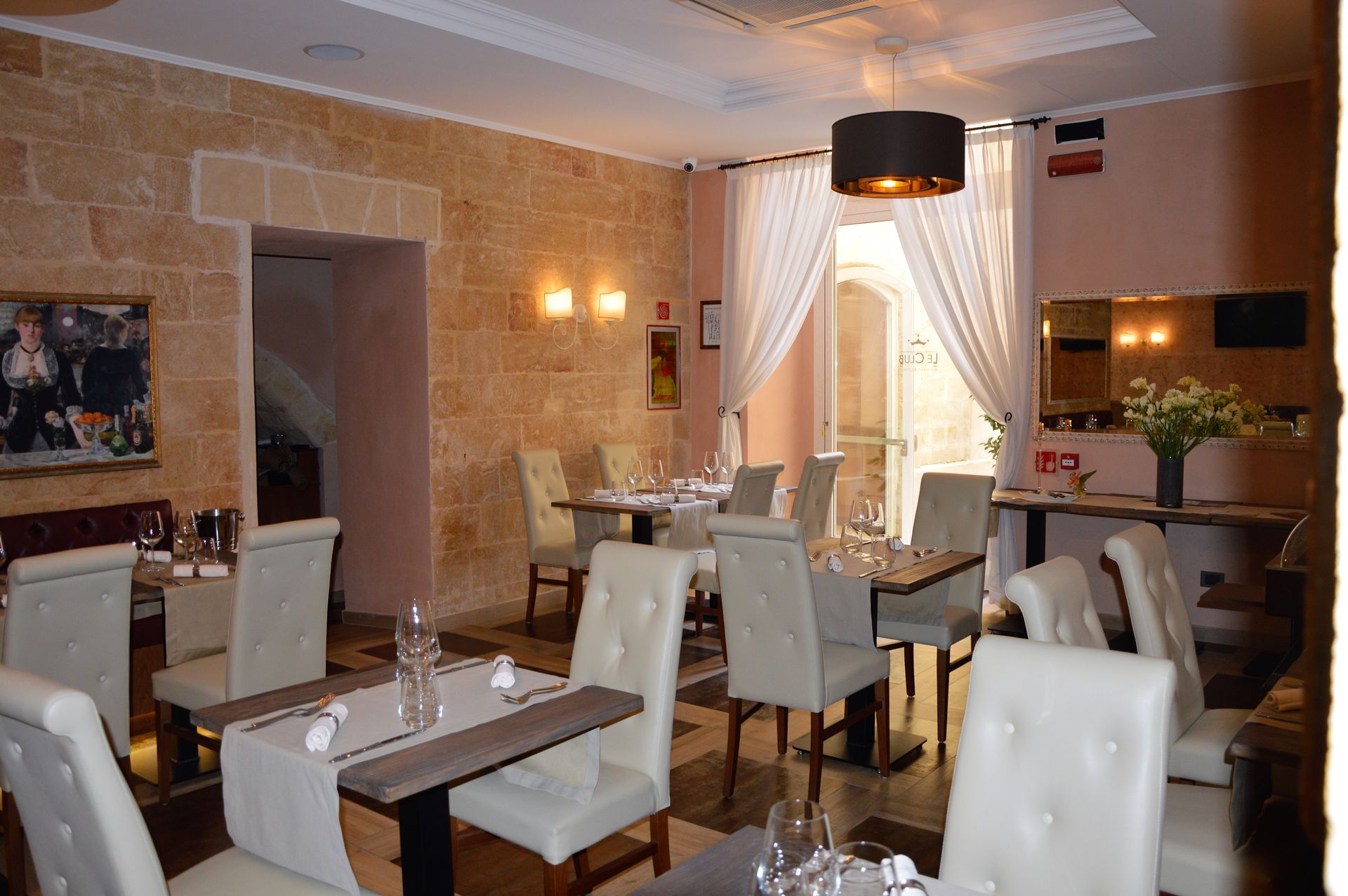 Restaurant dining room with tables set for service, stone walls, and draped doorway.