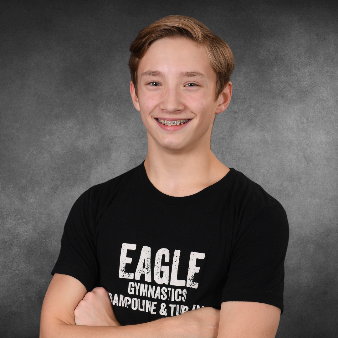 A young boy wearing an eagle gymnastics t-shirt with his arms crossed