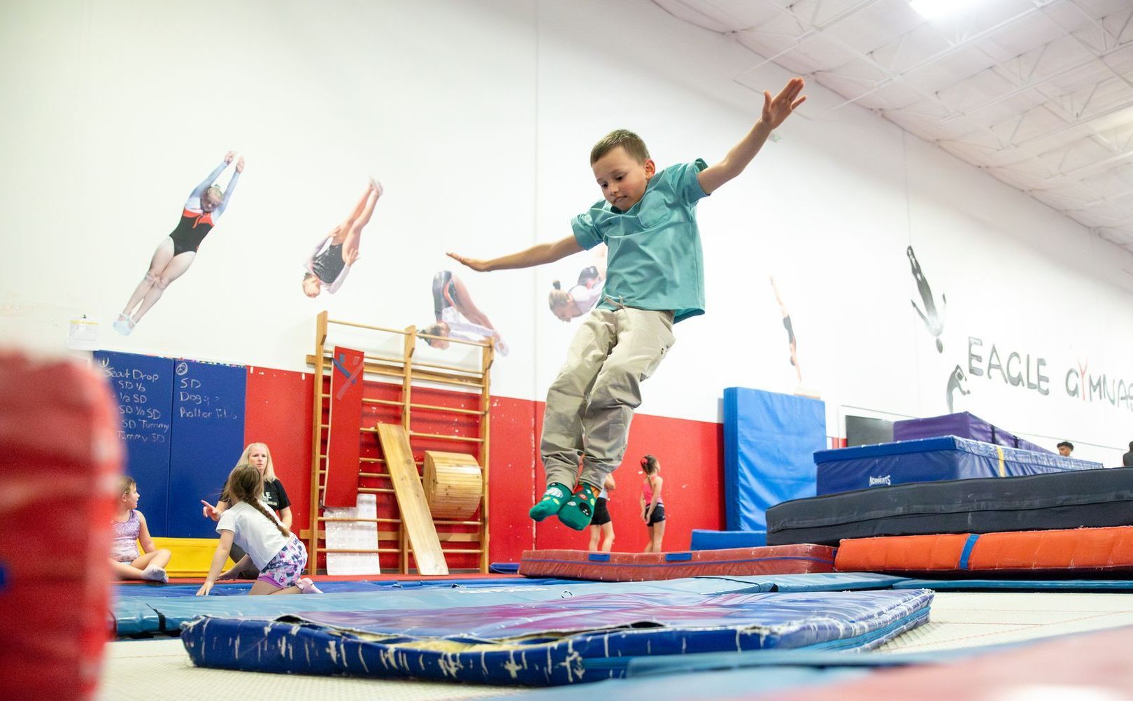 A girl is doing a handstand on a trampoline in a gym.