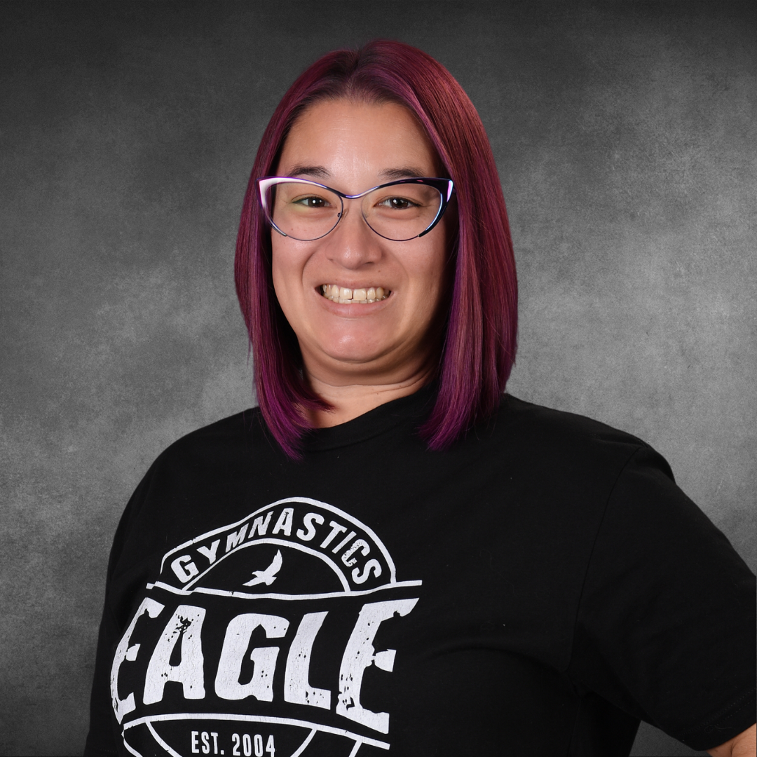 A woman with purple hair is wearing a black eagle gymnastics shirt