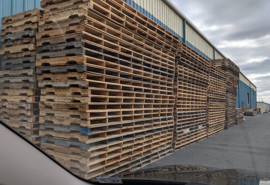A large stack of wooden pallets is sitting in front of a building.