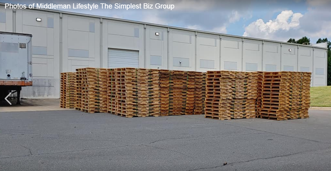 A large stack of wooden pallets in front of a building