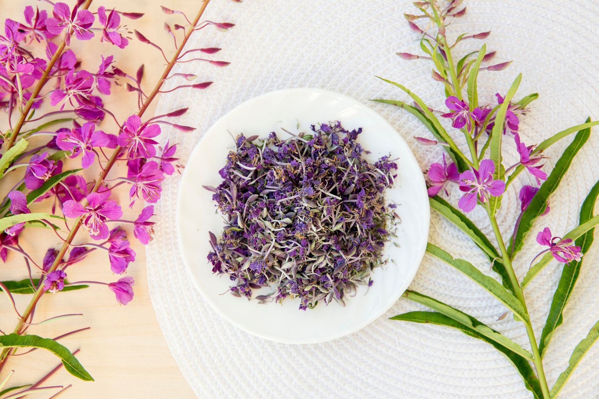 A white plate topped with dried purple flowers next to a bunch of purple flowers.