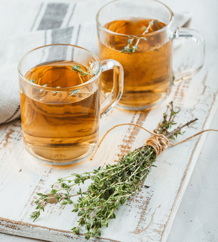 Two cups of tea with thyme on a wooden table.