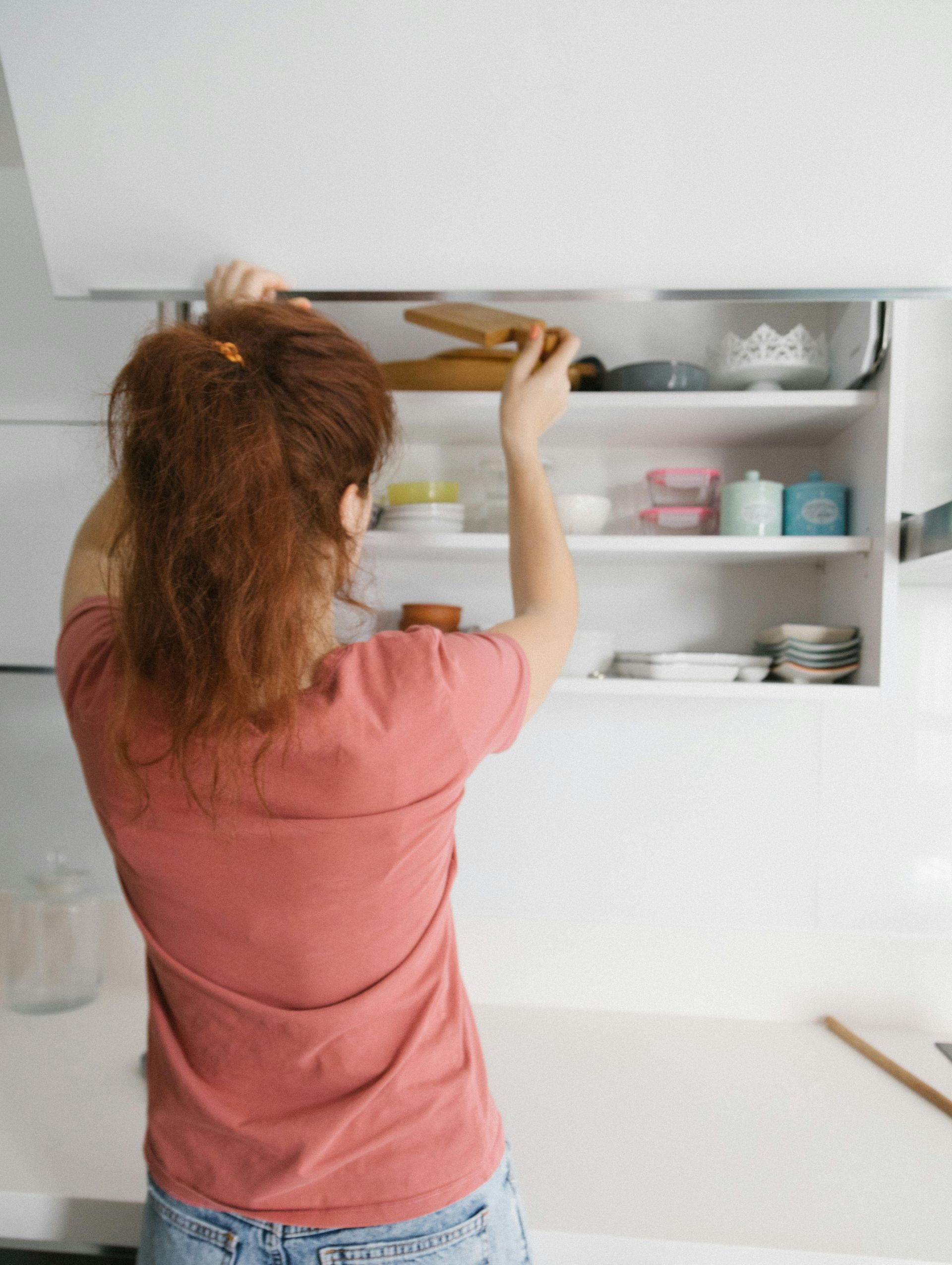Person reaching into white kitchen cabinet, retrieving items.