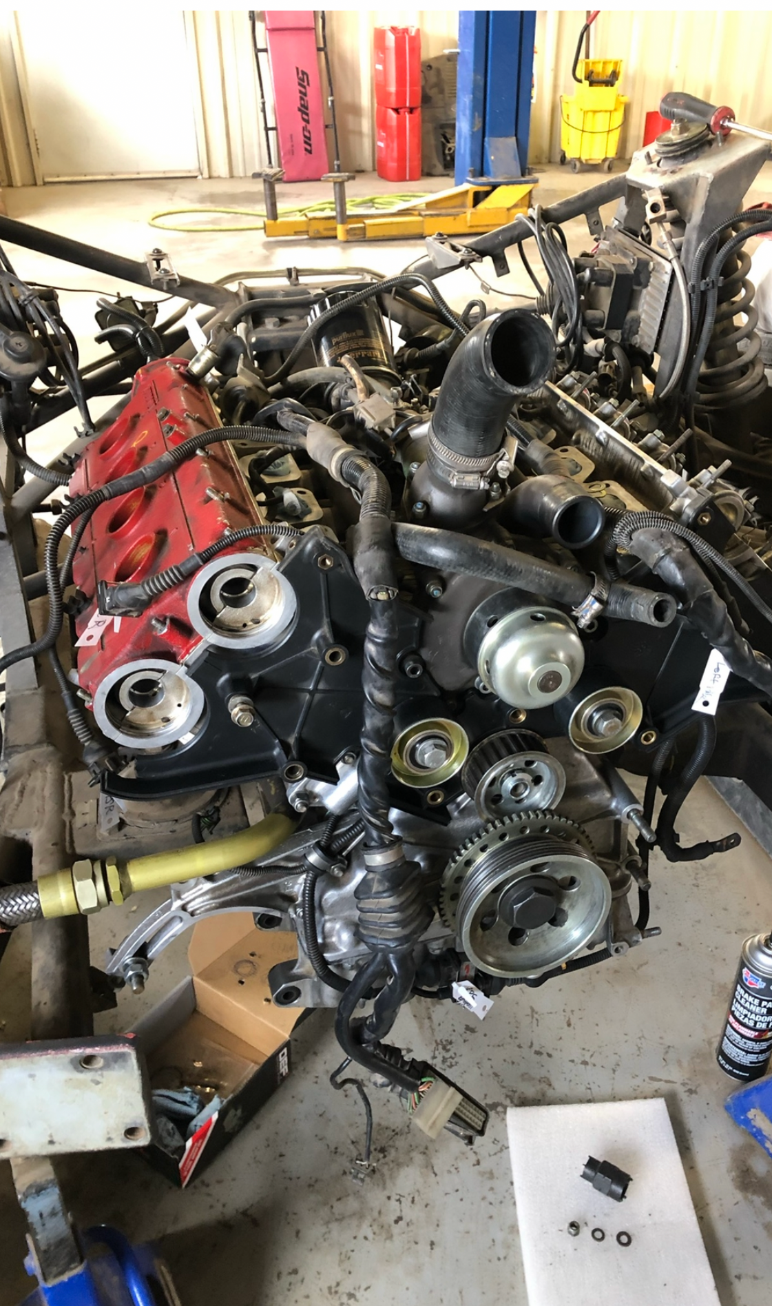 Engine partially disassembled; red valve covers, black engine components, and various tools in a garage setting.