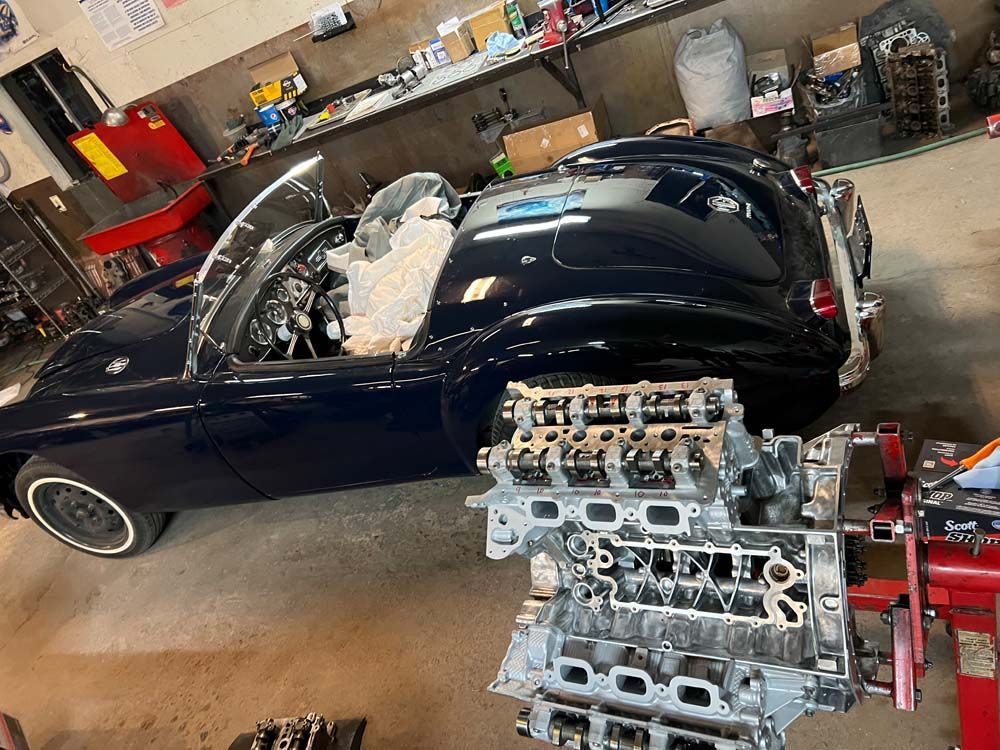A blue convertible car in a garage with a disassembled engine in the foreground.