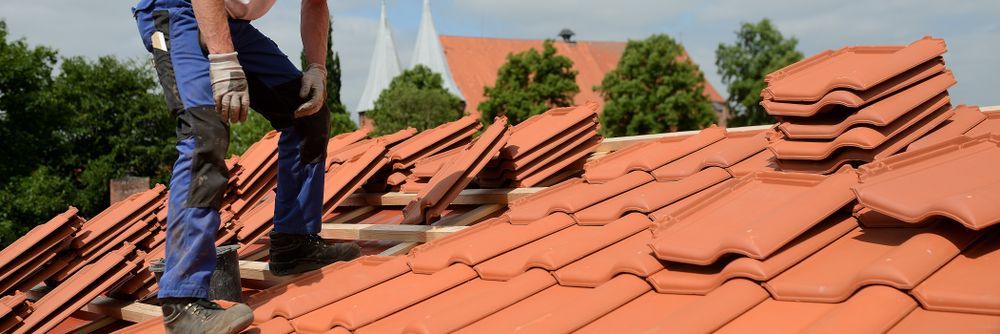 A Man is Standing on Top of a Tiled Roof — Roof Restoration Masters In Boolaroo, NSW