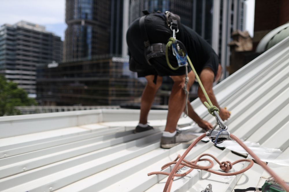 A Man is Working on the Roof of a Building — Roof Restoration Masters In Morisset, NSW