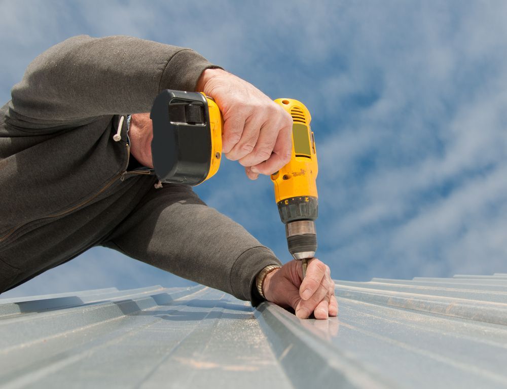 A Man is Working on a Roof With a Drill — Roof Restoration Masters In Boolaroo, NSW