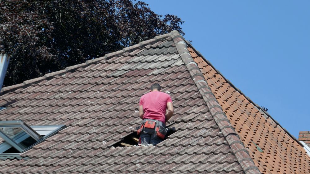A Man in a Red Shirt is Working on a Roof — Roof Restoration Masters In Rutherford, NSW