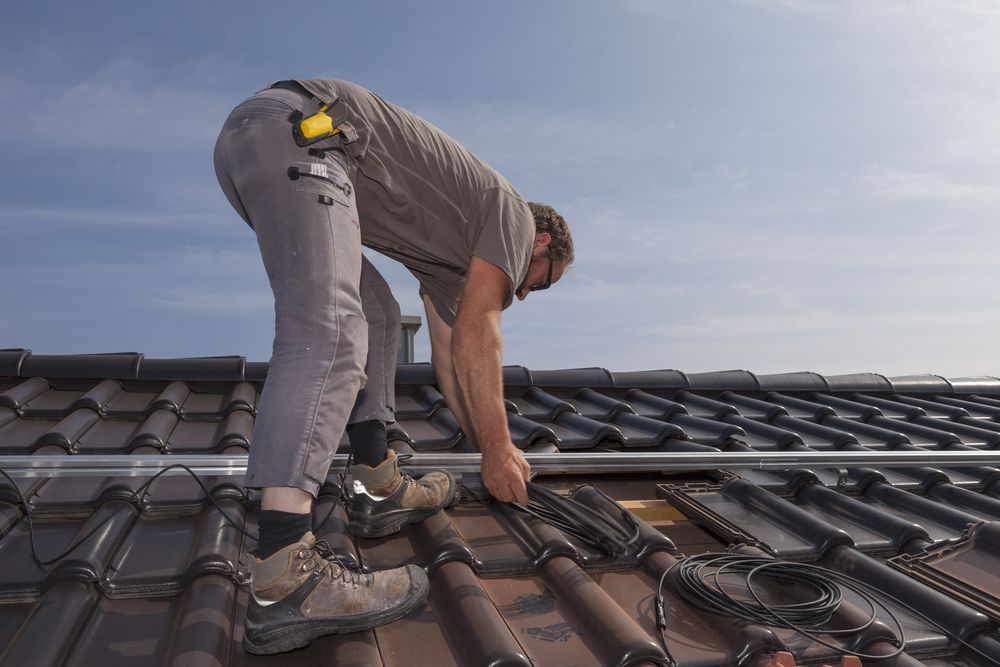 A Man is Installing Solar Panels on the Roof of a House — Roof Restoration Masters In Gosford, NSW