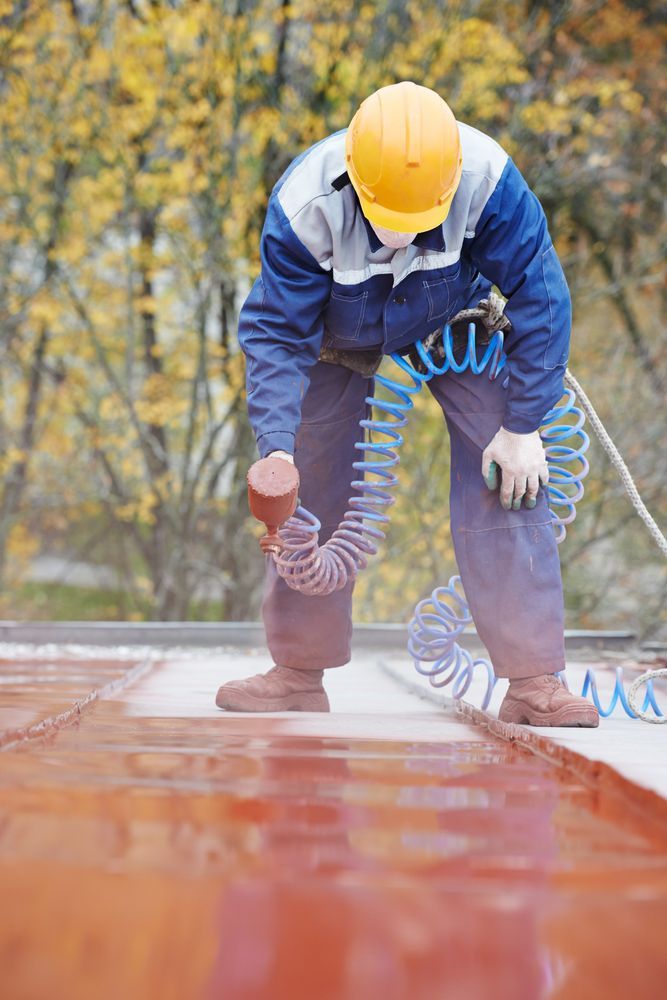 A Man in a Suit Spraying Paint on the Roof — Roof Restoration Masters In Boolaroo, NSW