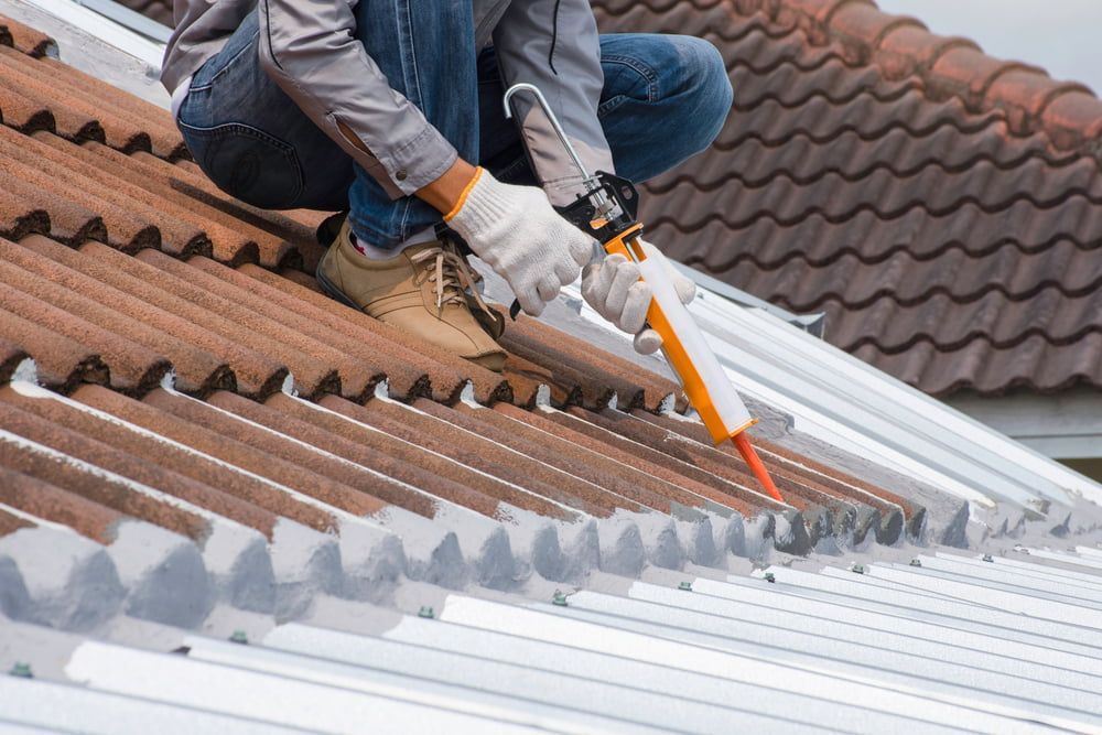 A Man is Applying Sealant to the Roof of a House — Roof Restoration Masters In Boolaroo, NSW
