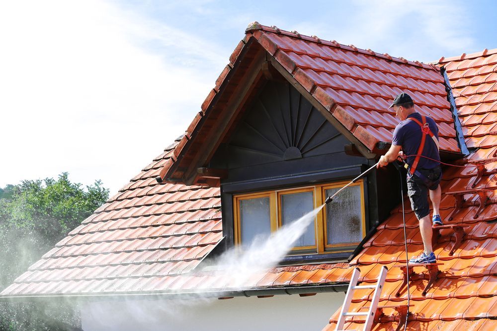 A Man is Using a High Pressure Washer to Clean a Roof — Roof Restoration Masters In Bonnells Bay, NSW