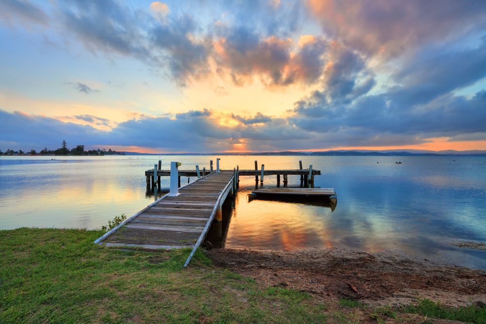 There is a Dock in the Middle of the Water at Sunset — Roof Restoration Masters In Belmont, NSW