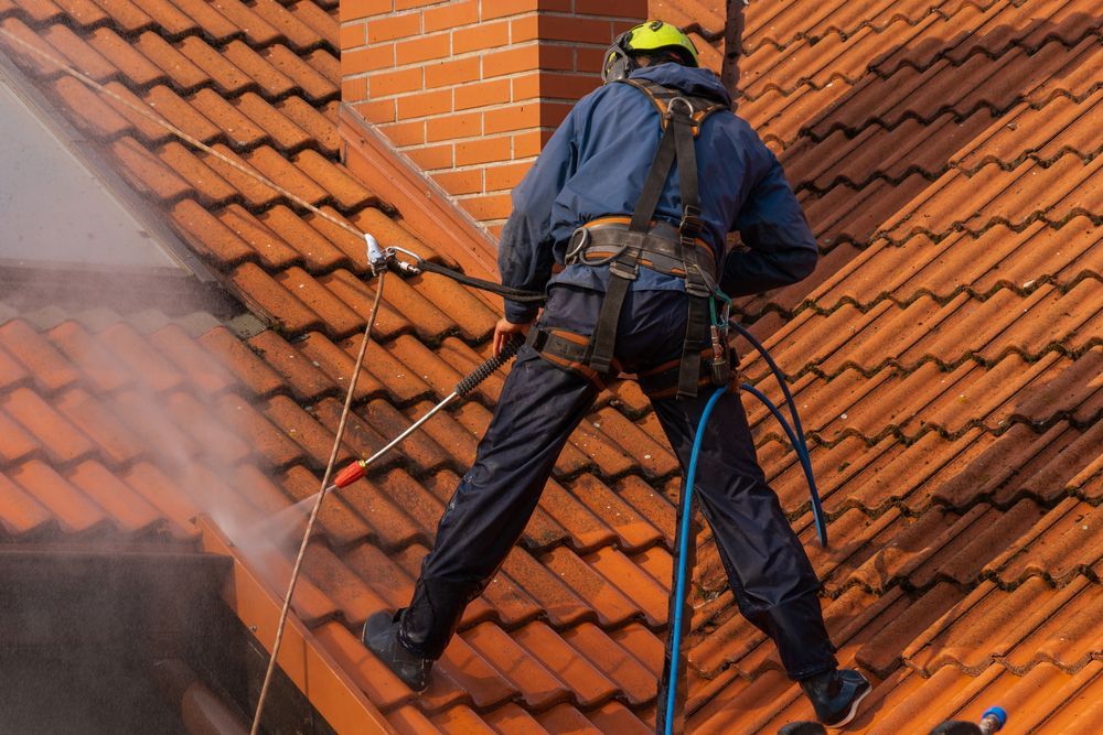 A Man is Cleaning a Roof With a High Pressure Washer— Roof Restoration Masters In Budgewoi, NSW