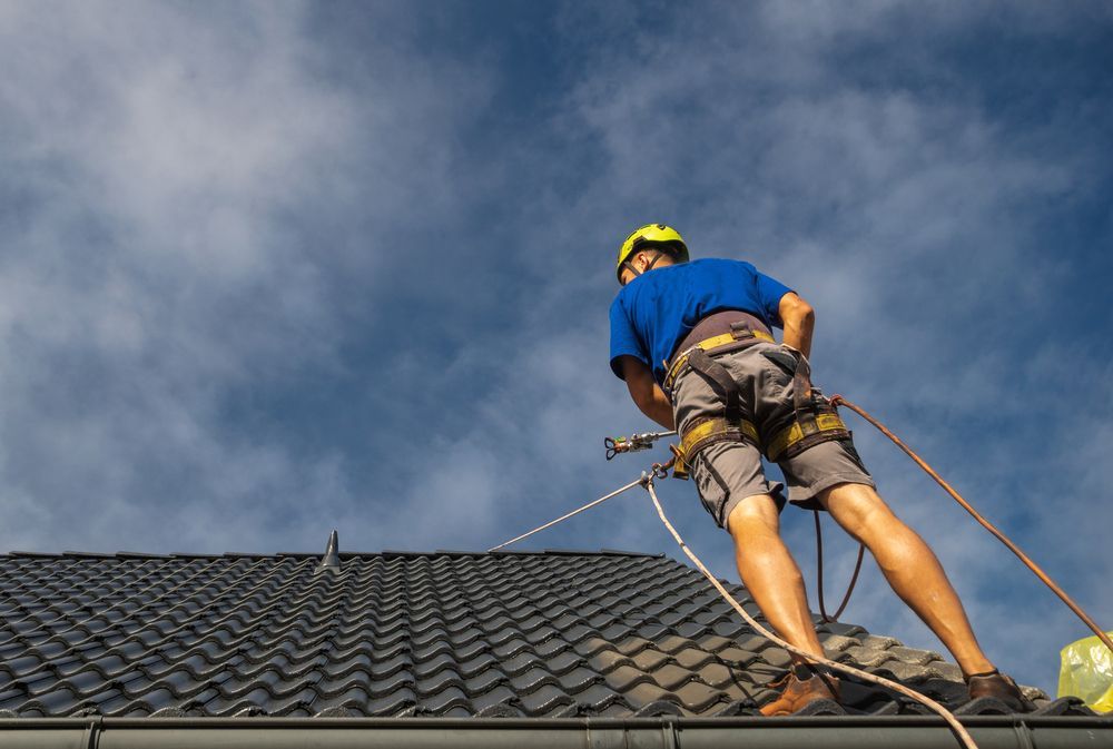 A Man is Spraying Paint on the Roof — Roof Restoration Masters In Boolaroo, NSW