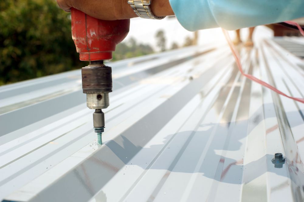 A Person is Using a Drill to Drill a Hole in a Metal Roof — Roof Restoration Masters In Boolaroo, NSW