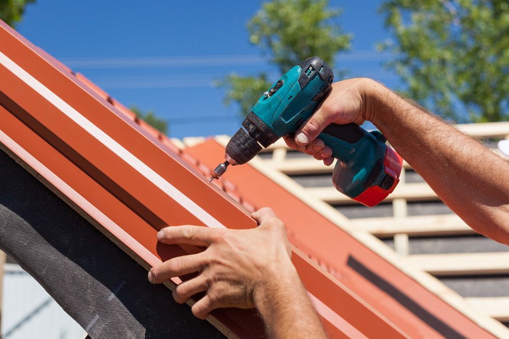 A Man is Working on a Roof With a Drill — Roof Restoration Masters In Newcastle, NSW