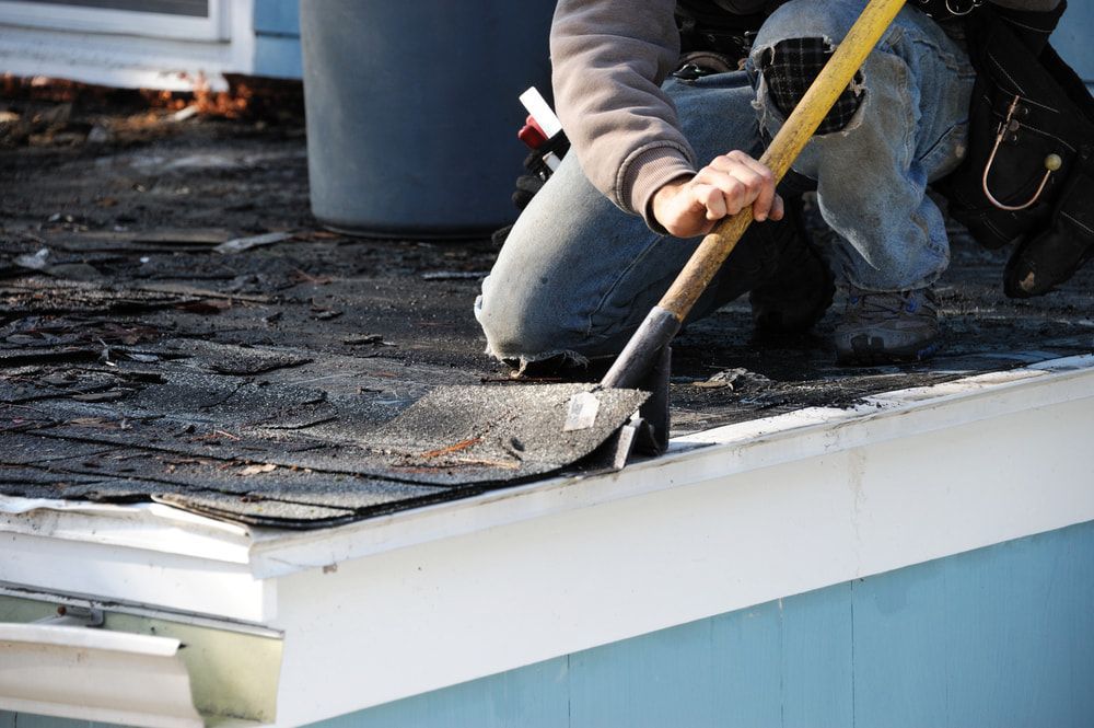 A Man is Using a Shovel to Remove Shingles From a Roof — Roof Restoration Masters In Newcastle, NSW