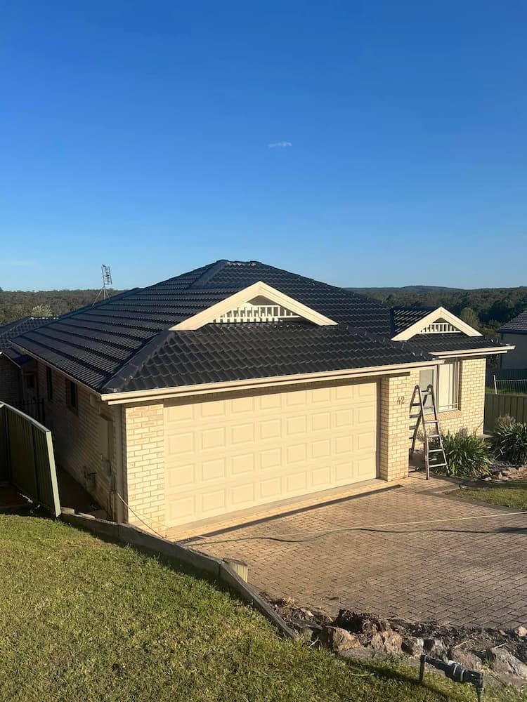 A House With a Black Roof and a Large Garage Door — Roof Restoration Masters In Bonnells Bay, NSW