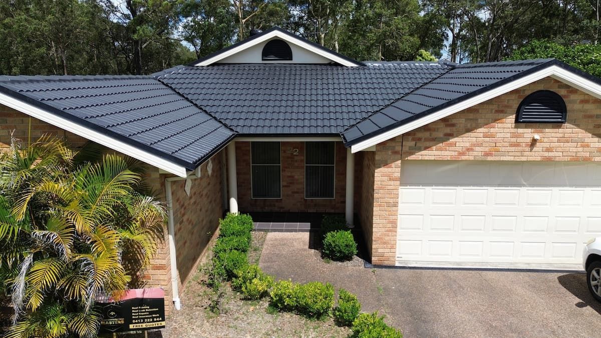 A Brick House With a Black Roof and a White Garage Door — Roof Restoration Masters In Fletcher, NSW