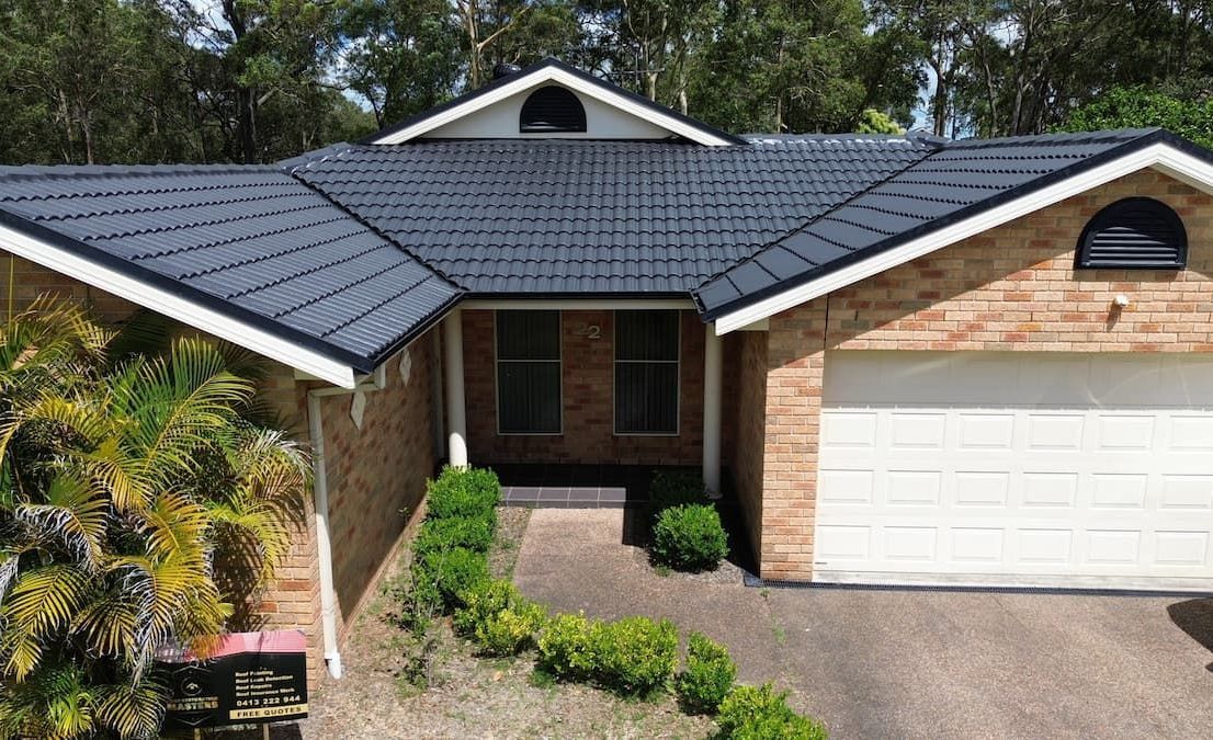 A Brick House With a Black Roof and a White Garage Door — Roof Restoration Masters In Morisset, NSW