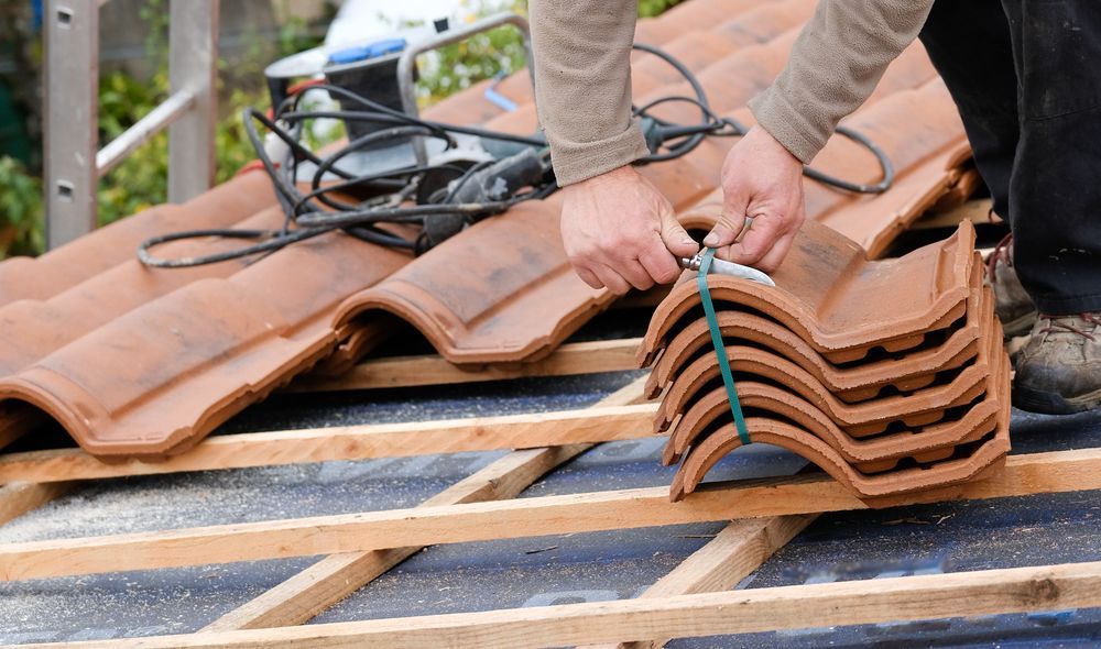 A Man is Laying Tiles on Top of a Wooden Frame on a Roof — Roof Restoration Masters In New Lambton, NSW