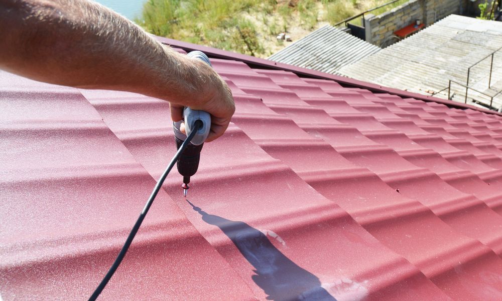 A Person is Using a Drill on a Red Roof — Roof Restoration Masters In Morisset, NSW