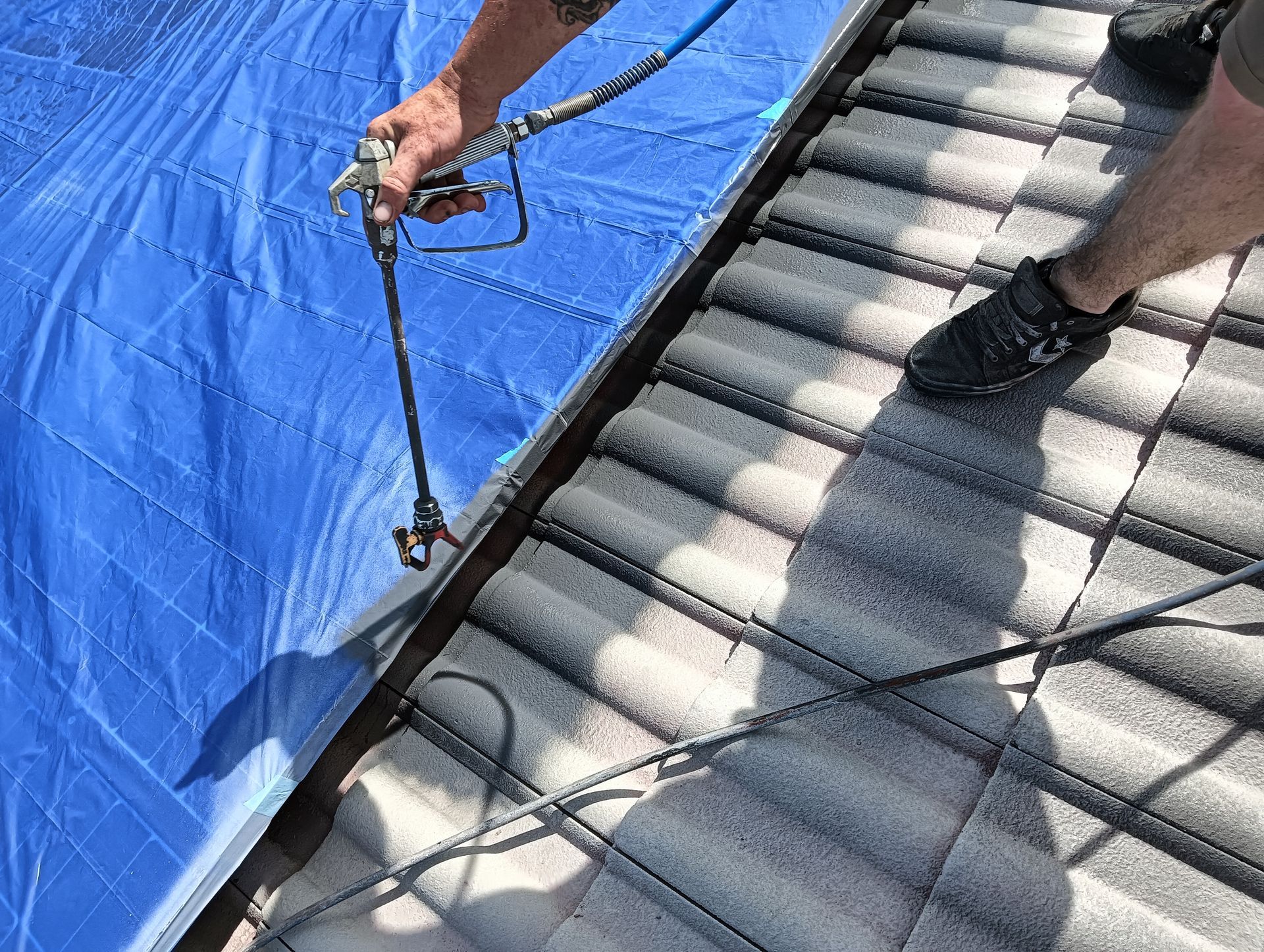 A Man is Spraying a Blue Tarp on a Roof — Roof Restoration Masters In Morisset Park, NSW