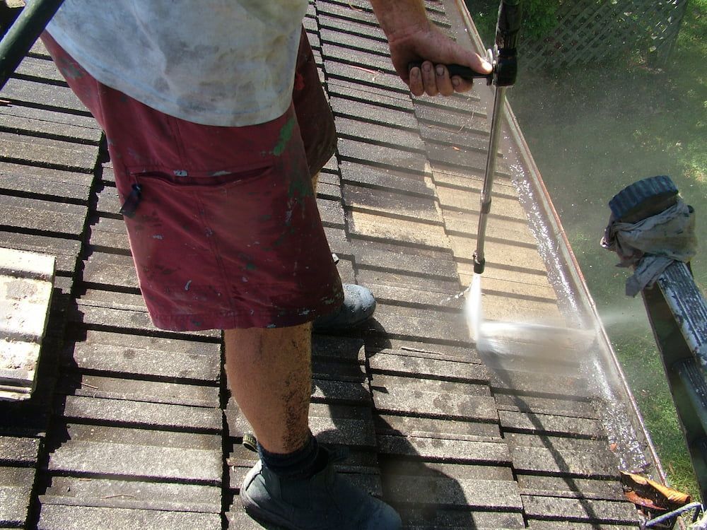 A Man is Using a High Pressure Washer to Clean a Roof — Roof Restoration Masters In Morisset Park, NSW
