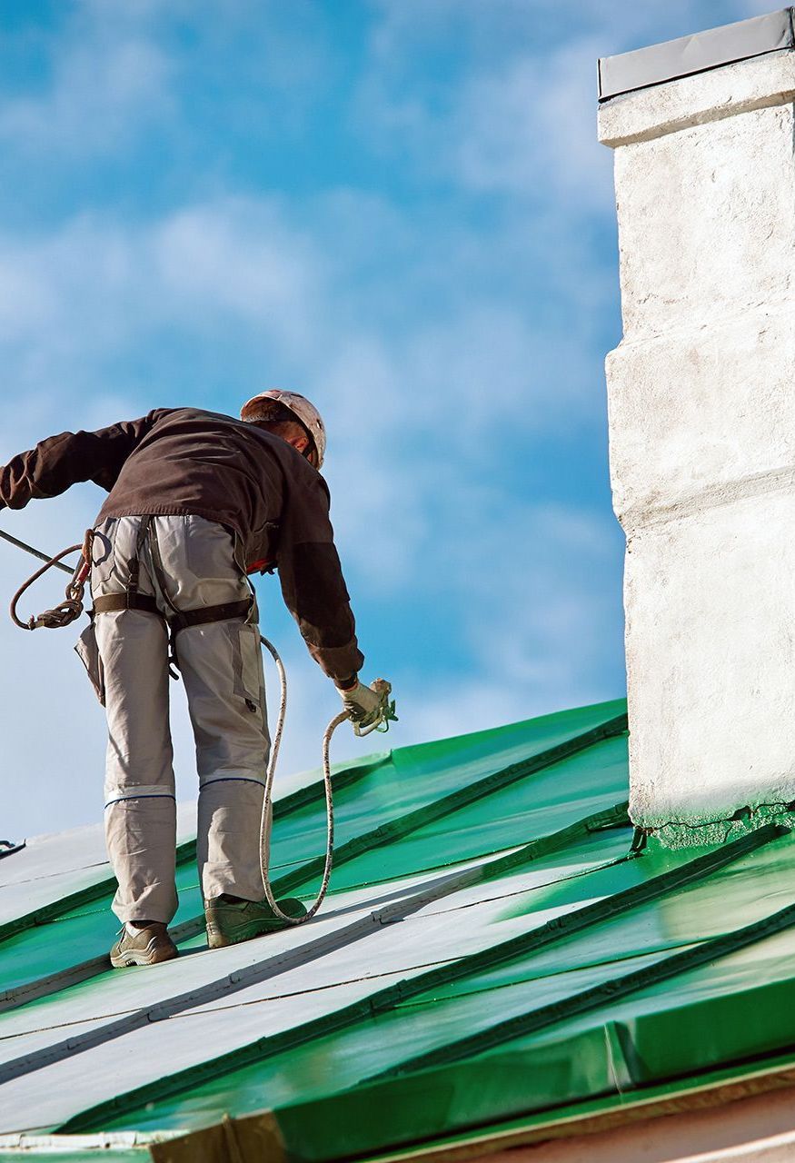 A Man is Painting the Roof of a Building With a Sprayer — Roof Restoration Masters In Cameron Park, NSW